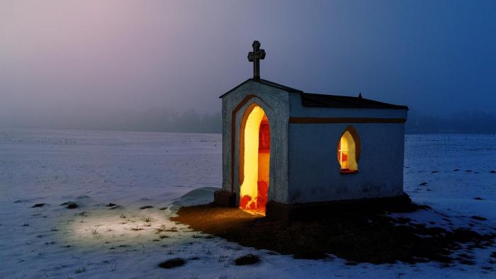 A cross on the roof of a house with a bright light inside